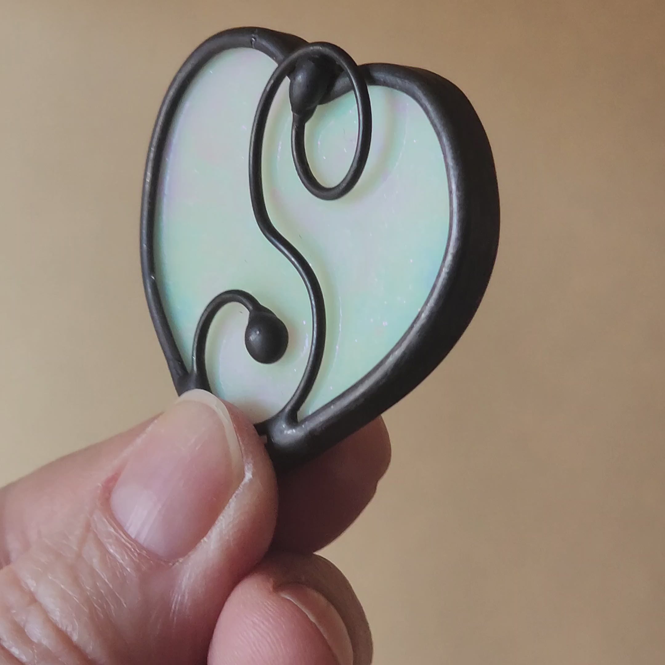 White iridescent heart with hand shaped wire scroll shimmering in sunlight, on a neutral background